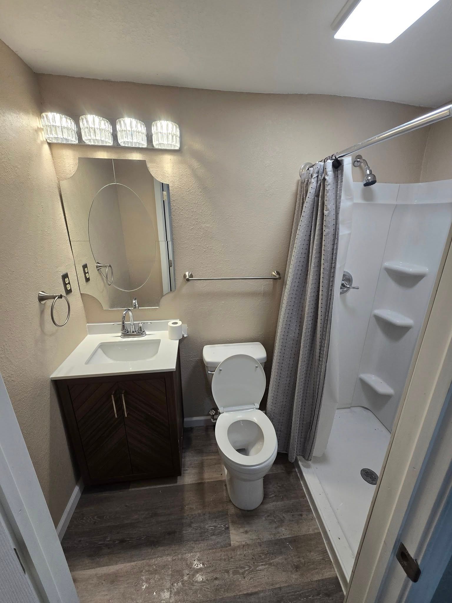 Small bathroom with vanity, mirror, toilet, and shower curtain in beige and gray tones