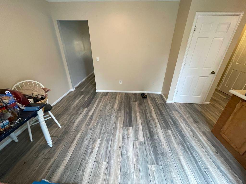 Empty room with gray wood-look flooring, beige walls, white doors, and a chair at left.