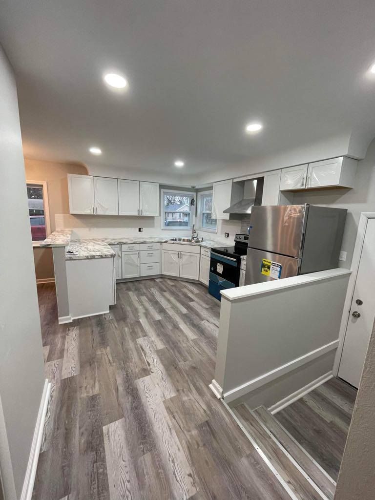 Bright modern kitchen with white cabinets, stainless appliances, gray wood floors, and a small stair railing.