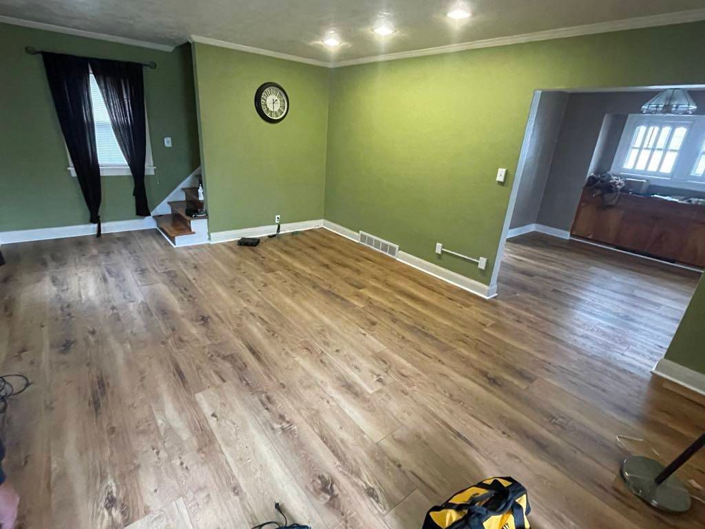 Empty living room with green walls, wood floors, and an open doorway to a dining area