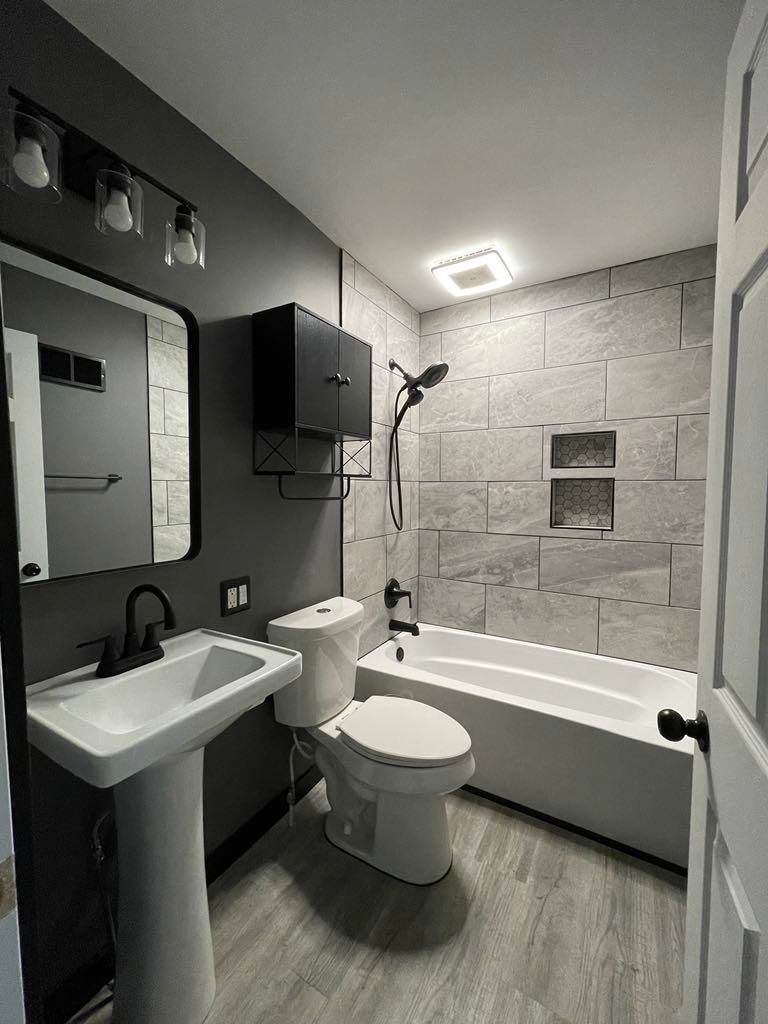 Modern gray-and-black bathroom with sink, toilet, tub, shower, and wall mirror