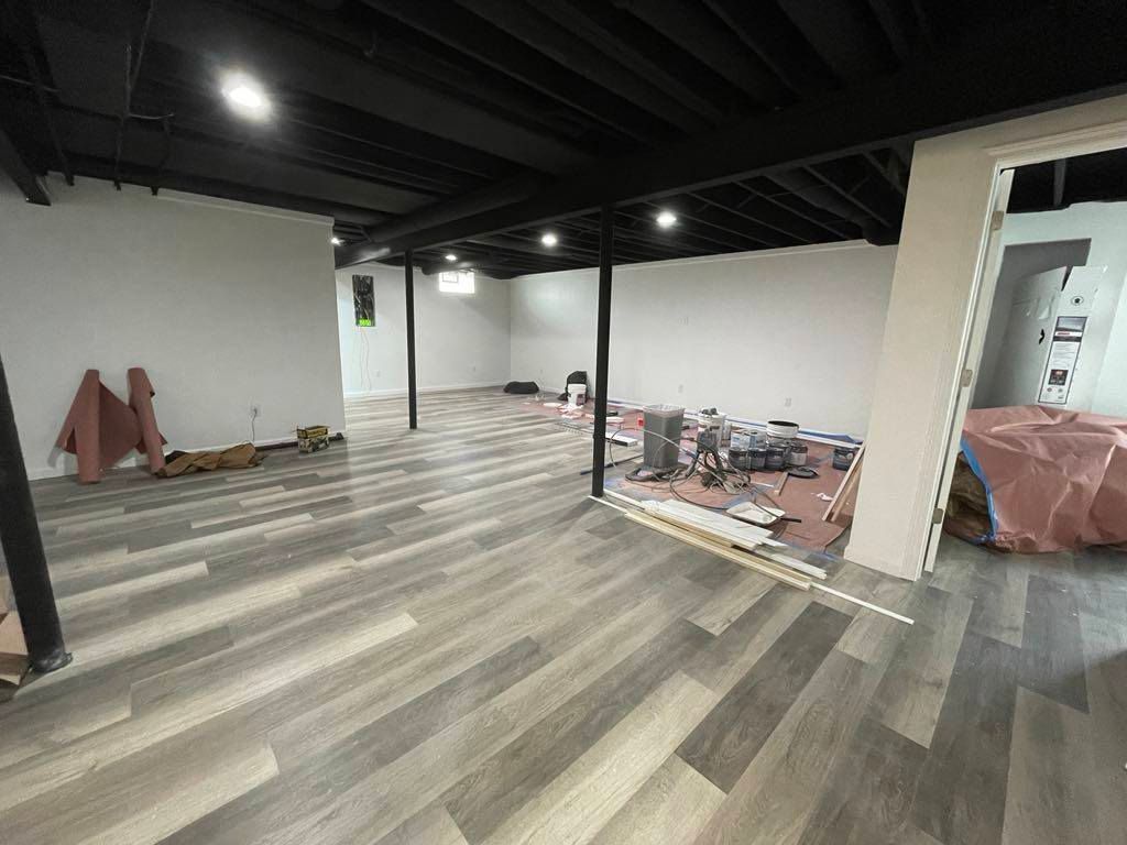 Vacant room under renovation with gray wood floors, black ceiling, white walls, and construction materials scattered around