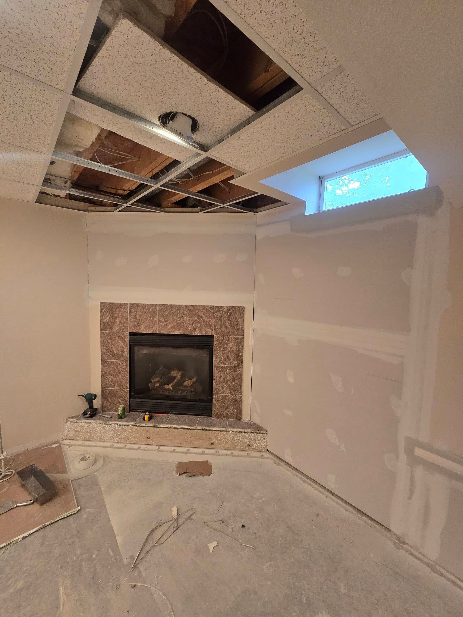 Partially renovated living room with exposed ceiling, fireplace, and patched drywall
