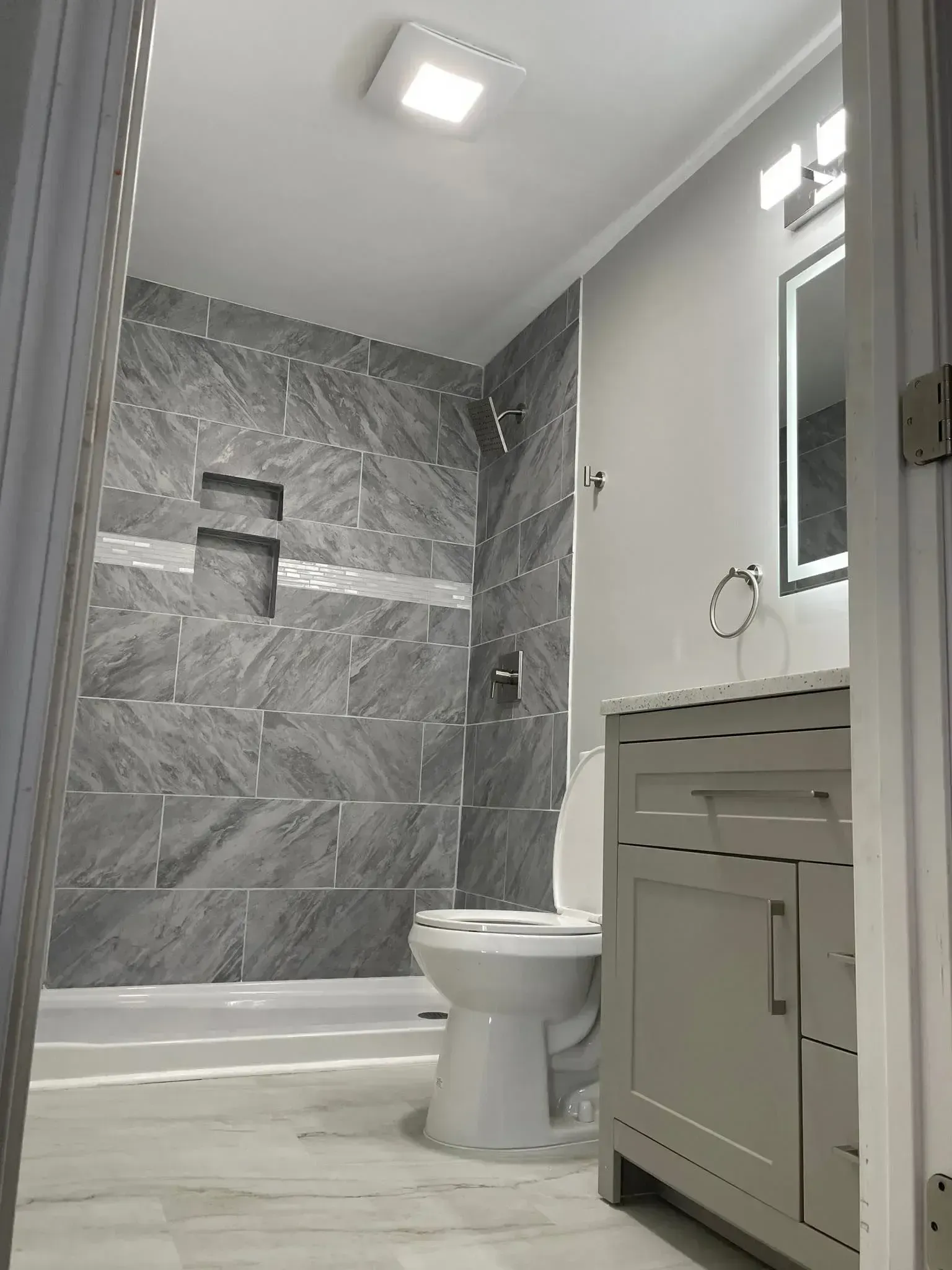 White shower stall with grab bar, handheld showerhead, and blue floor suction mats in a bathroom