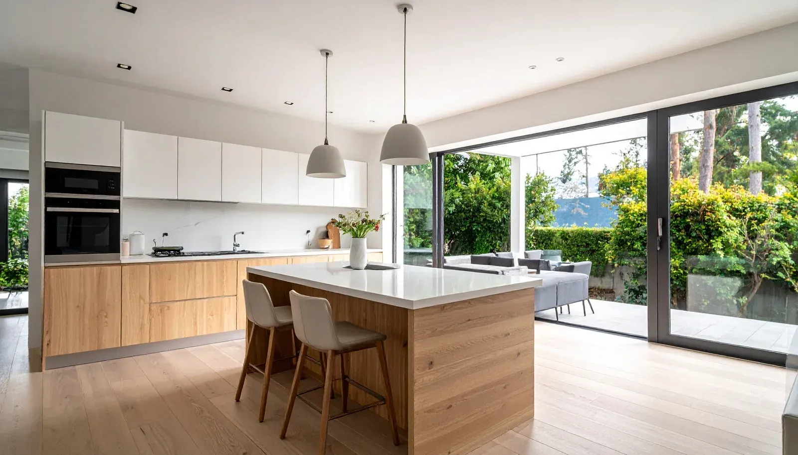 Modern kitchen with wooden island, white cabinets, and large glass doors opening to a garden
