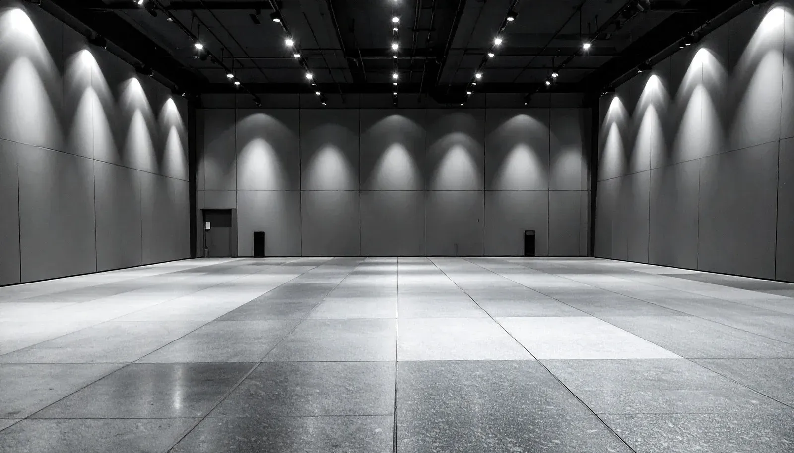 Empty gray exhibition hall with bright overhead spotlights and a polished tiled floor
