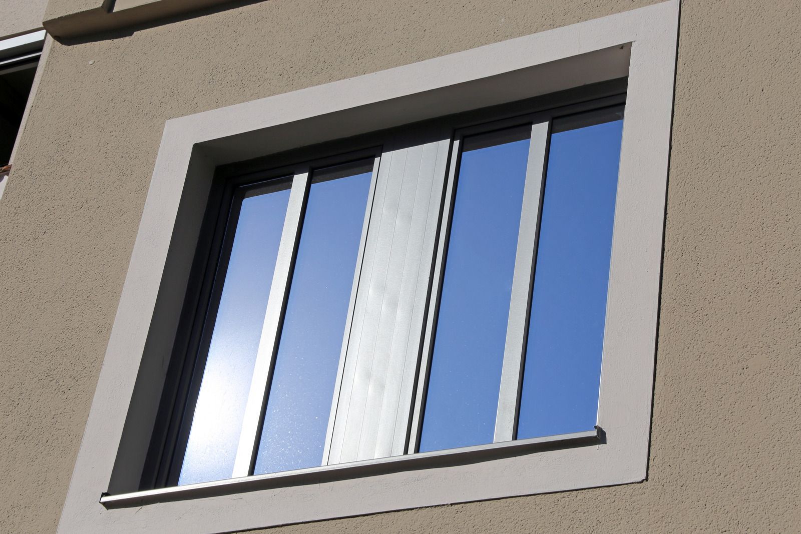 Close-up of a building window with blue sky reflections and a partially open white blind