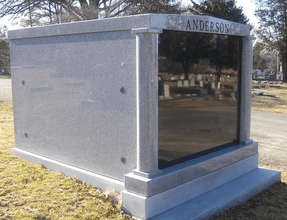 Large gray granite mausoleum in a cemetery; black glass door; “ANDERSON’S” engraved on top.