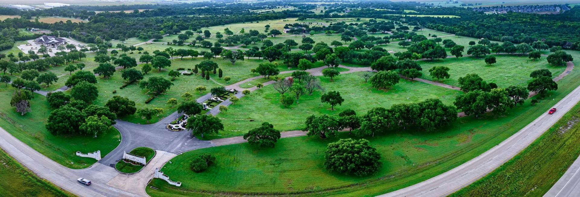 Aerial view of a green park with trees and two roads, a car is on the right road.