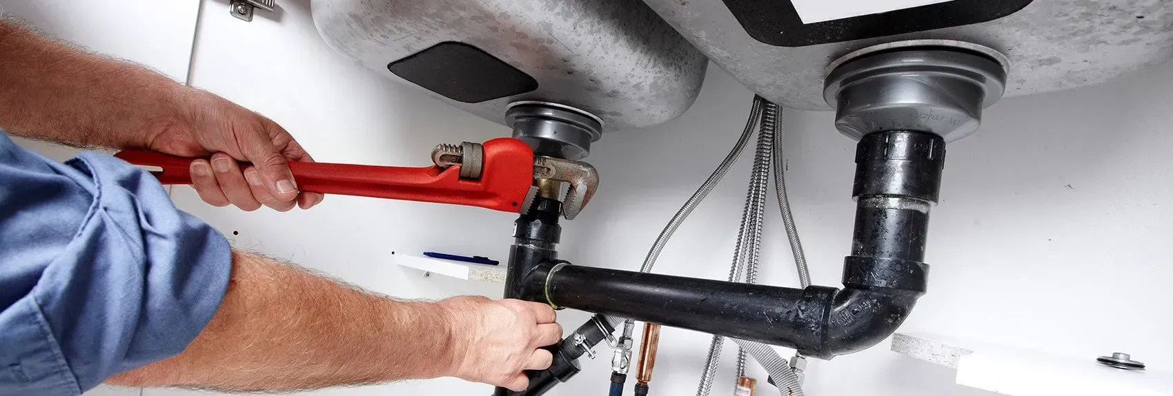 A Plumber Using a Red Wrench on a Black Pipe Under a Sink — Harwood Plumbing & Gasfitting Pty Ltd in Alawa, NT