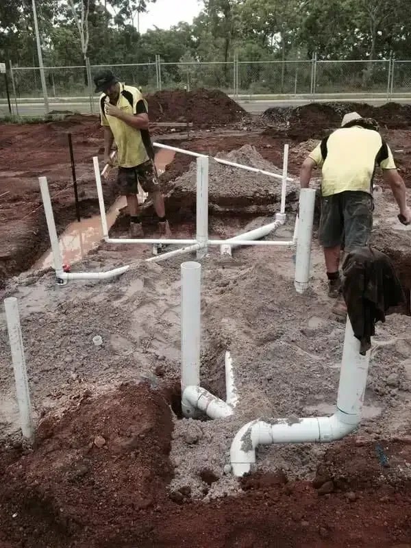 Two Workers Installing White Plumbing Pipes in a Dirt Construction Site — Harwood Plumbing & Gasfitting Pty Ltd in Alawa, NT