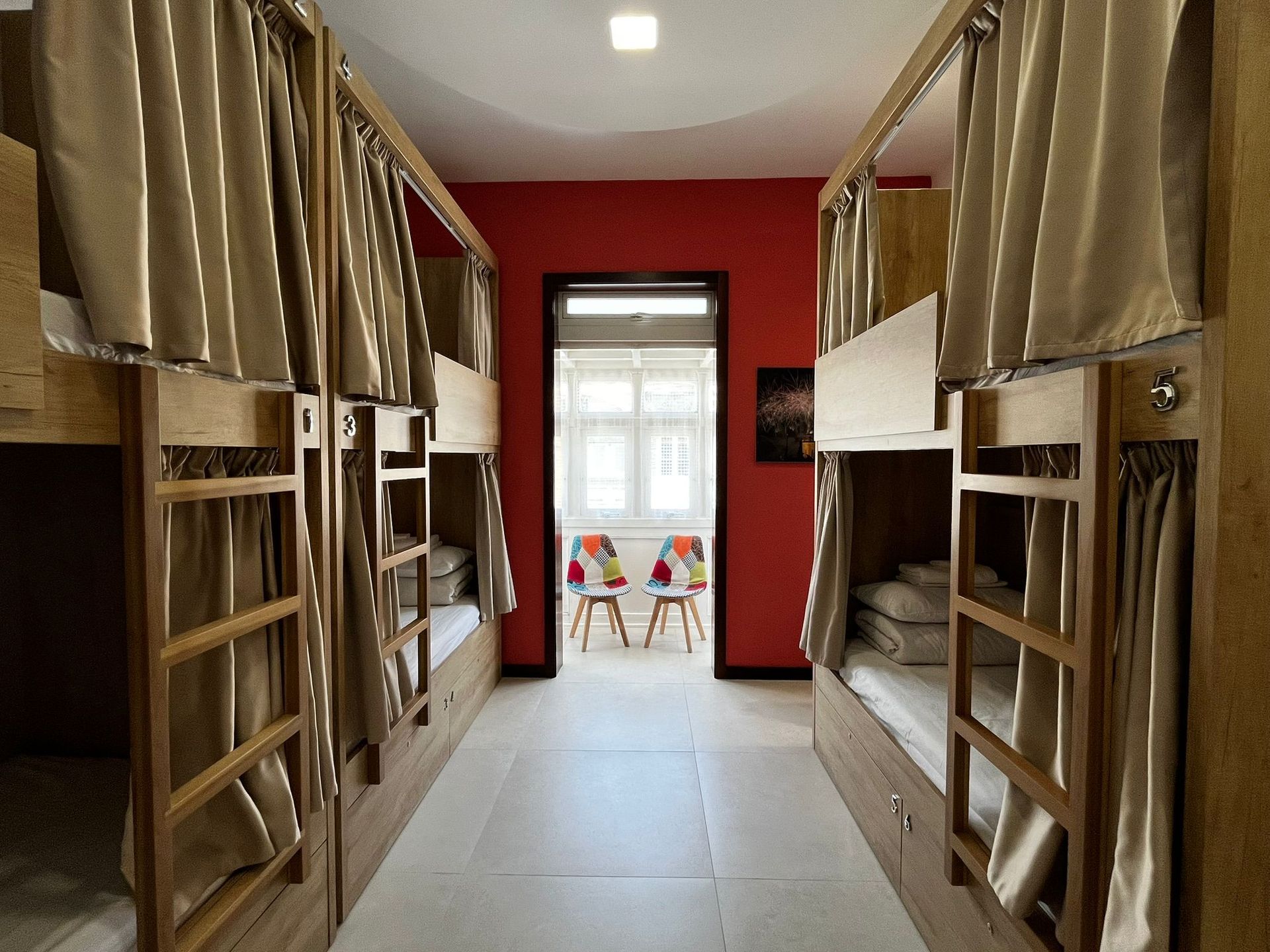 Dormitory-style room with two rows of bunk beds, red accent wall, chairs & a Maltese Balcony. 