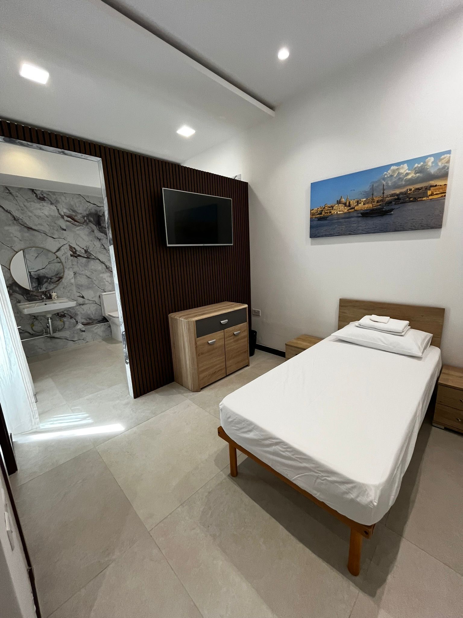 Modern room with single bed, wall-mounted TV, dresser, and cityscape artwork