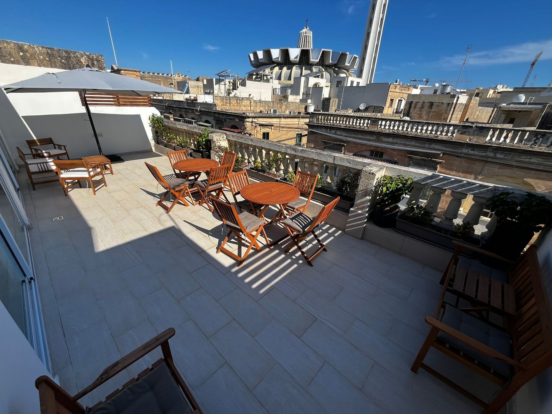 Rooftop terrace with orange tables and chairs, white pergola, and city buildings under a clear blue sky