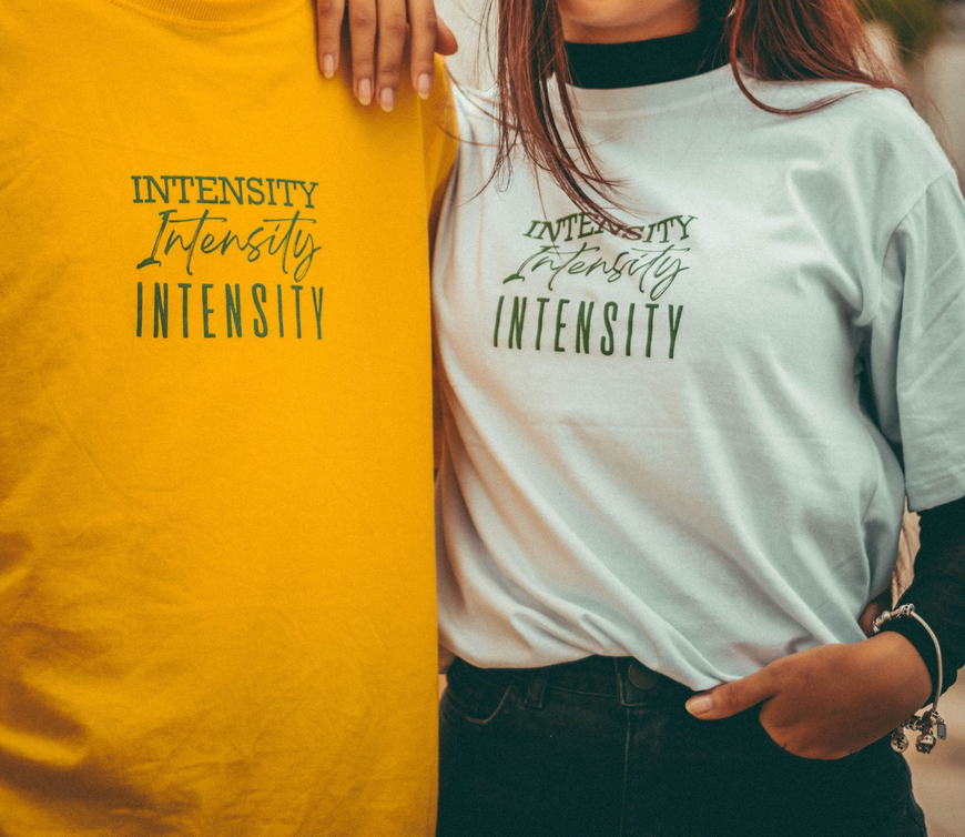 Two people wearing matching INTENSITY shirts, one yellow and one mint green, standing together.