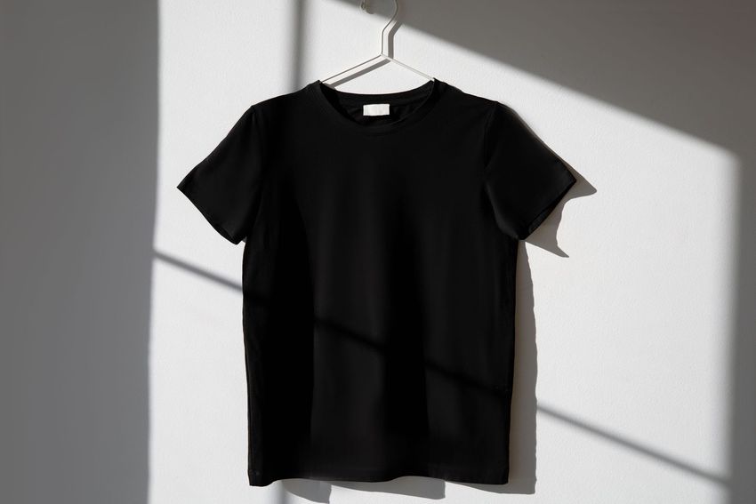 Black T-shirt hanging on a hanger against a sunlit wall
