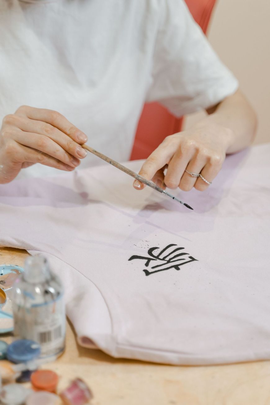 Hands using tweezers to place a black design on a white T-shirt at a worktable