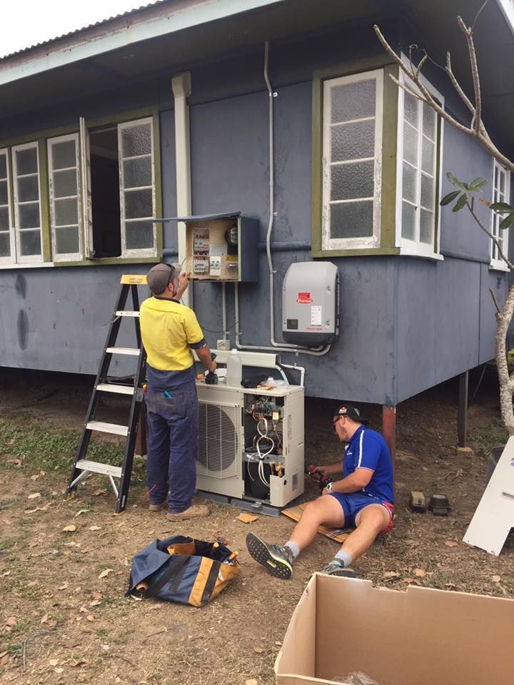 Two Men Are Working on an Air Conditioner Outside of a Blue House — Legit Air Conditioning & Refrigeration in Garbutt, QLD