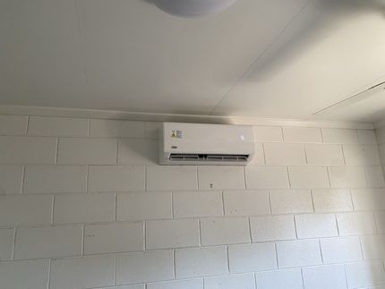 A White Air Conditioner is Mounted on a White Brick Wall — Legit Air Conditioning & Refrigeration in Garbutt, QLD