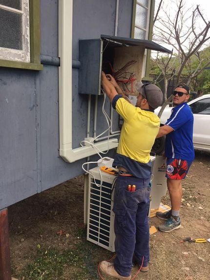 Two Men Are Working on an Air Conditioner Outside of a Building — Legit Air Conditioning & Refrigeration in Garbutt, QLD