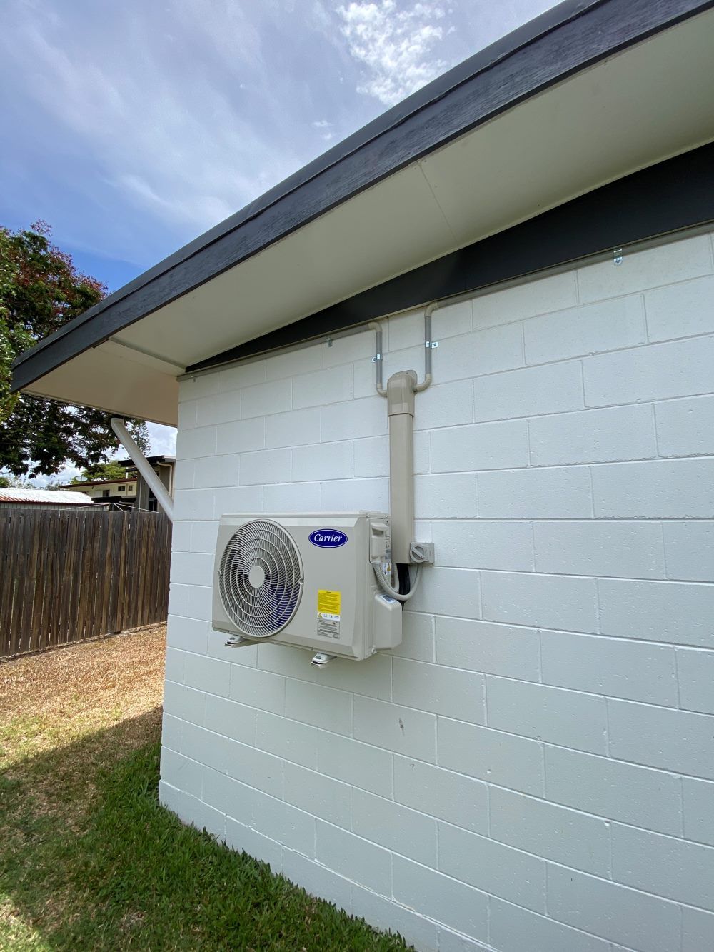A White Brick Building With a Fan on the Side of It — Legit Air Conditioning & Refrigeration in Garbutt, QLD
