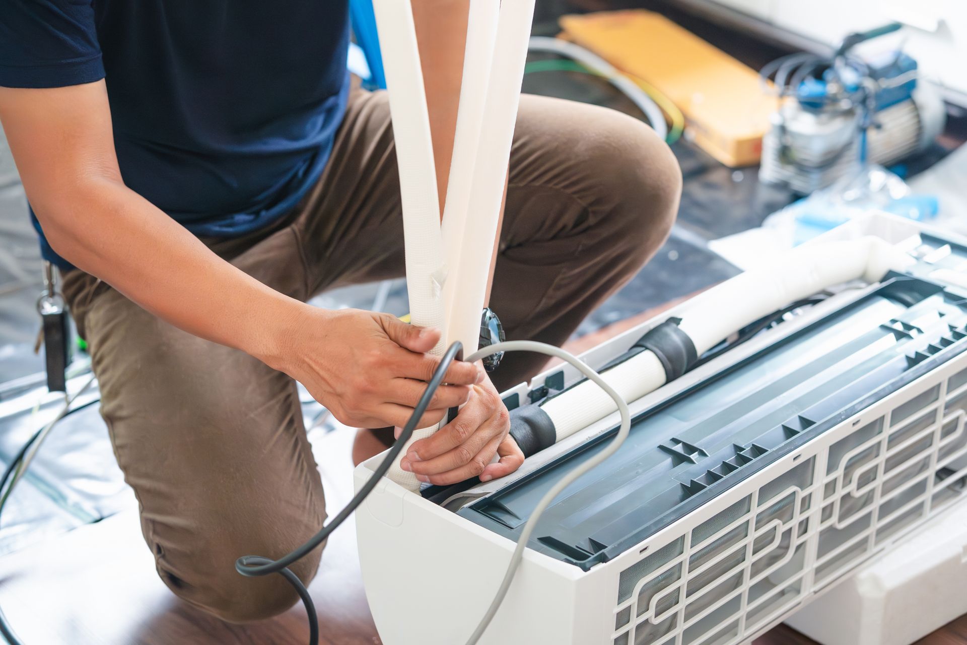 A Man is Kneeling Down to Fix an Air Conditioner — Legit Air Conditioning & Refrigeration in Garbutt, QLD