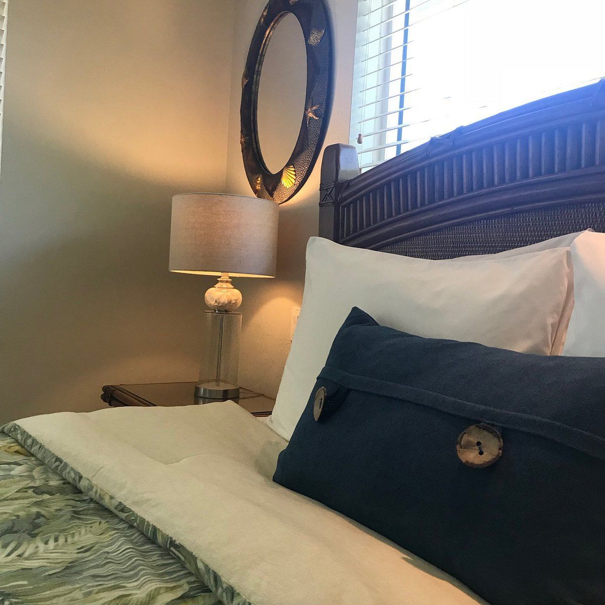 Cozy bedroom corner with a bed, white pillows, dark bolster, bedside lamp, and round wall mirror