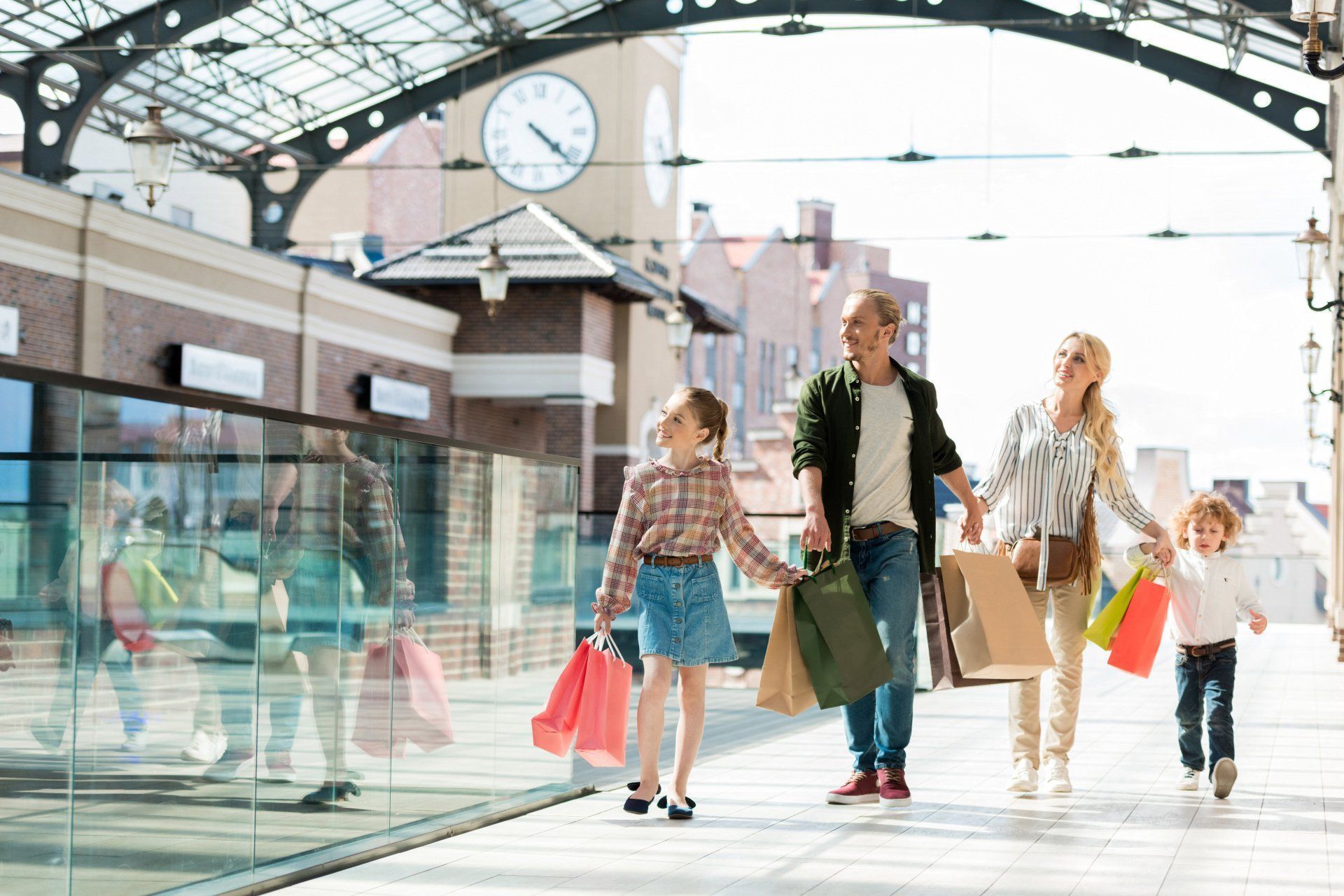 Shoppers walking through a bright indoor mall with glass railings and a clock overhead