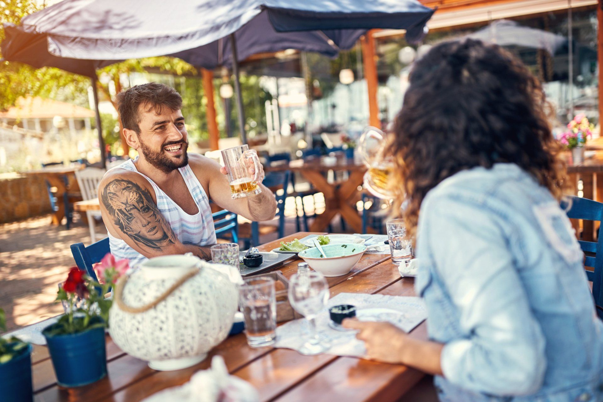 People chatting at an outdoor café, with drinks and plates on a sunny patio.