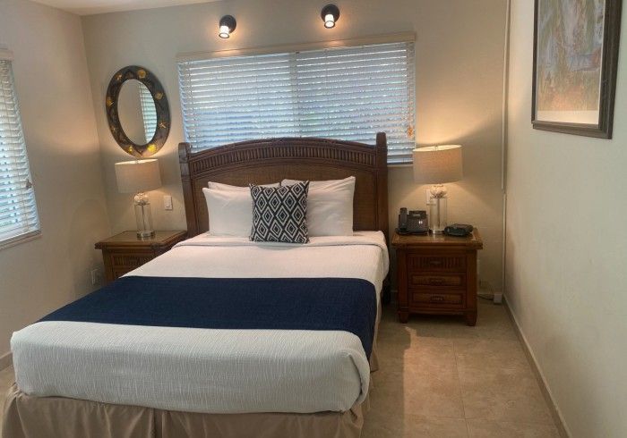 Bedroom with a neatly made bed, dark blue runner, wooden headboard, lamps, and wall art.