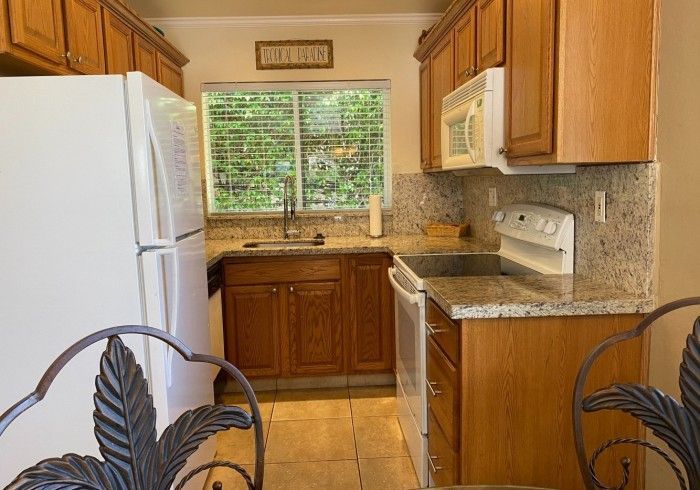 Small kitchen with white appliances, wood cabinets, granite counters, and a window over the sink.