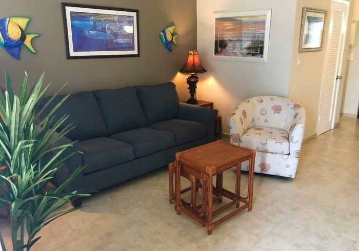 Cozy living room with navy sofa, floral armchair, wooden nesting tables, lamp, and potted plant.
