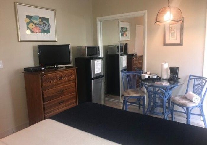 Small room with a dresser, TV, mini fridge, table with chairs, and a bed in the foreground.