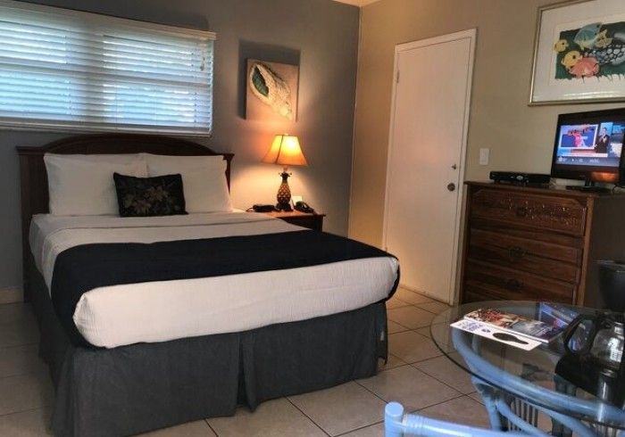 Bedroom with neatly made bed, bedside lamp, dresser, TV, and a glass coffee table.
