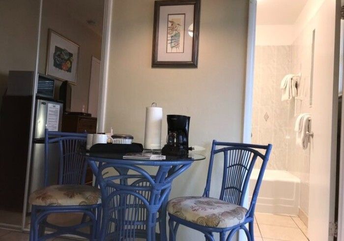 Small kitchen dining area with blue chairs, round table, coffee maker, and a view into a bathroom.