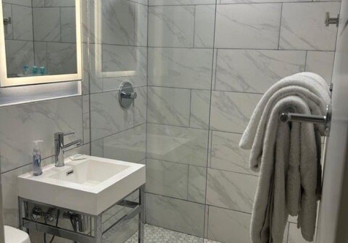 Modern bathroom with white sink, tiled walls, glass shower, and gray towels on a rack