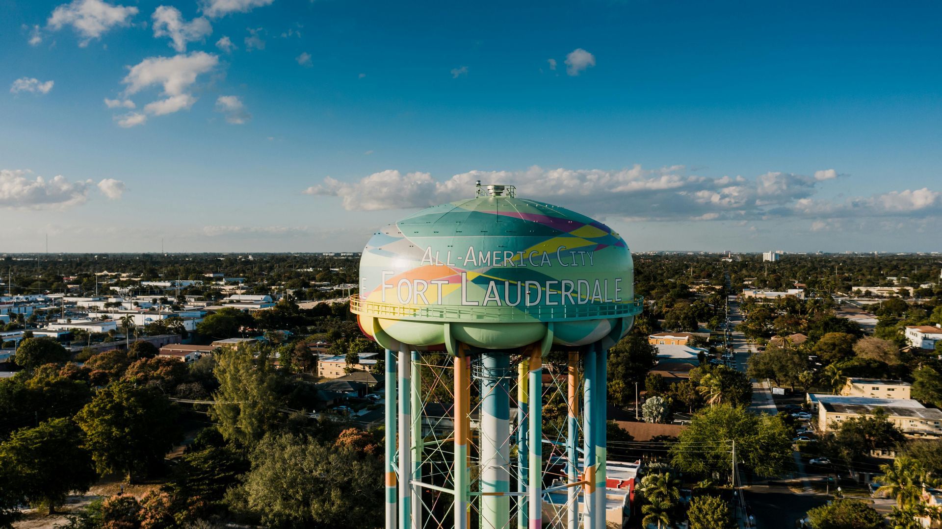 Sky-blue water tower with colorful mural above a suburban neighborhood under a sunny sky