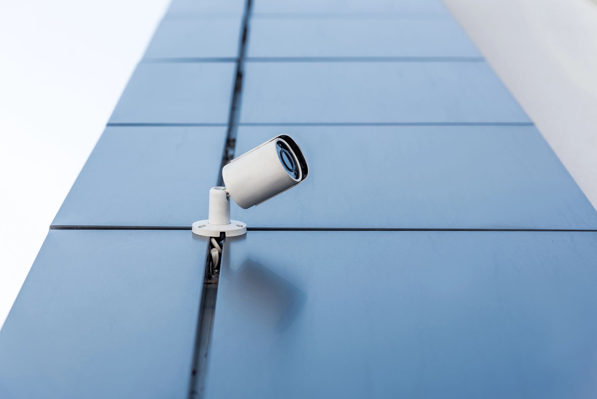 Telecamera di sicurezza bianca montata su una parete blu, inclinata verso il basso