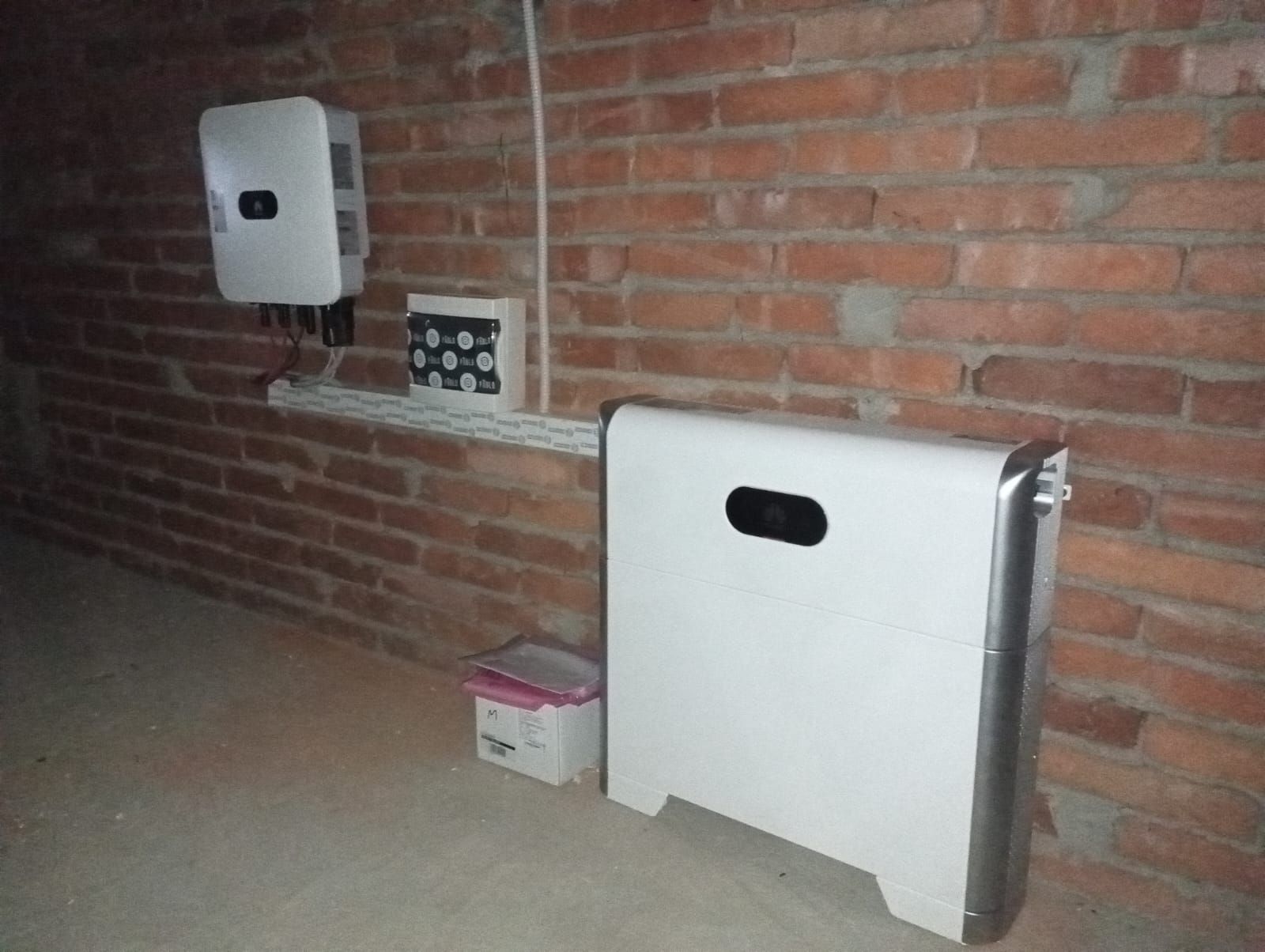 Ambiente interno con una parete di mattoni, due dispenser bianchi fissati alla parete e un paravento o pannello pieghevole bianco.