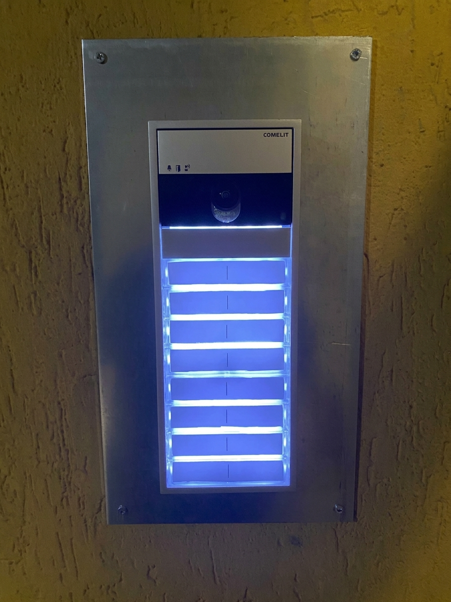 Pannello di controllo a parete illuminato di blu, con barre orizzontali luminose all’interno di una cornice metallica