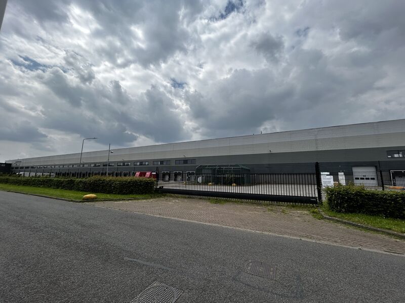 Een groot gebouw met een hek eromheen en een bewolkte lucht op de achtergrond.