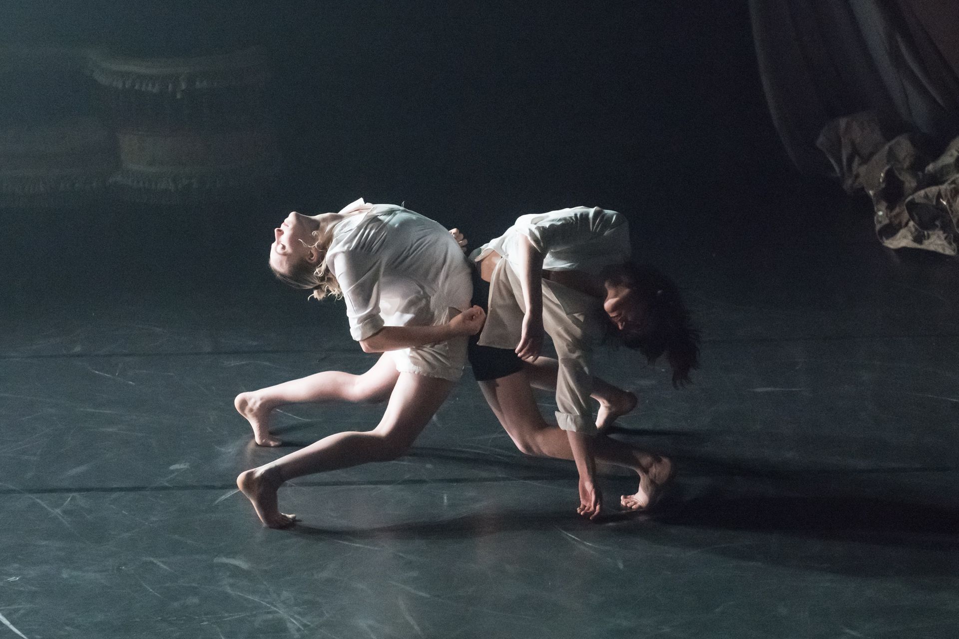 Two circus artists in white blouses arch their backs with stomachs touching each other.