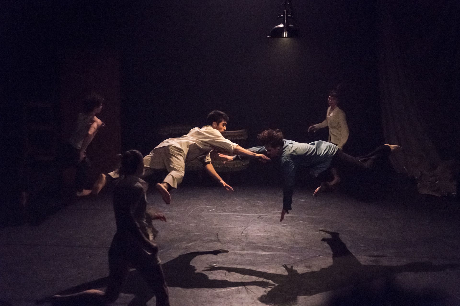 Two artists leap in the air parallel to the ground in dynamic lighting. Others run around them.
