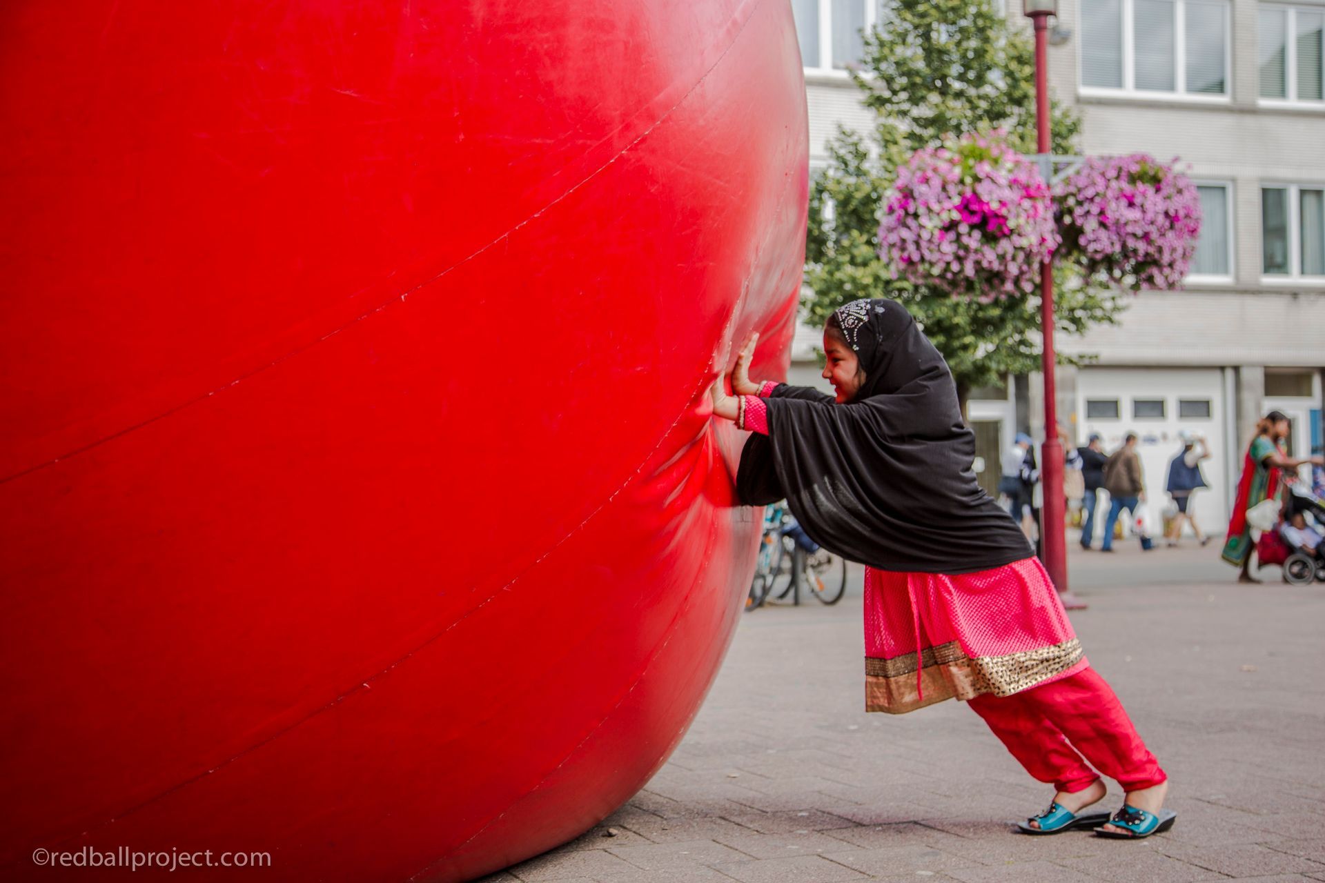 A person pushes against a large red inflatable ball outdoors.