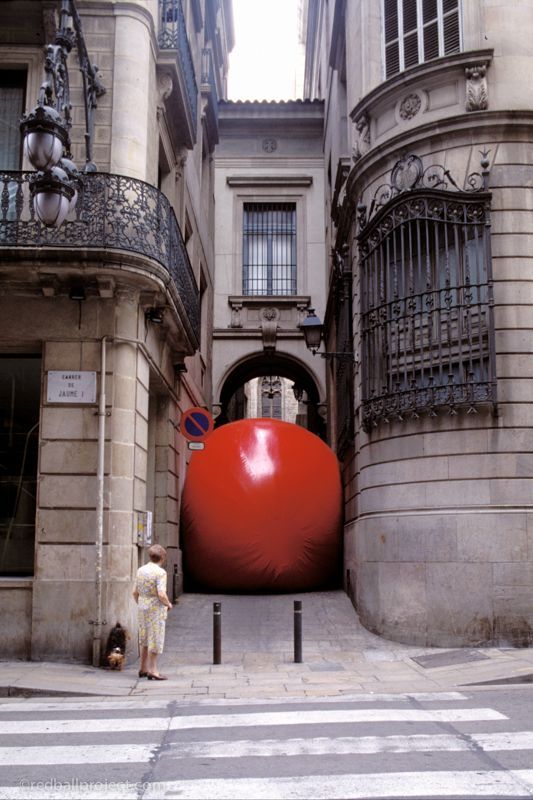 A large red inflatable ball squeezes into an alleyway.