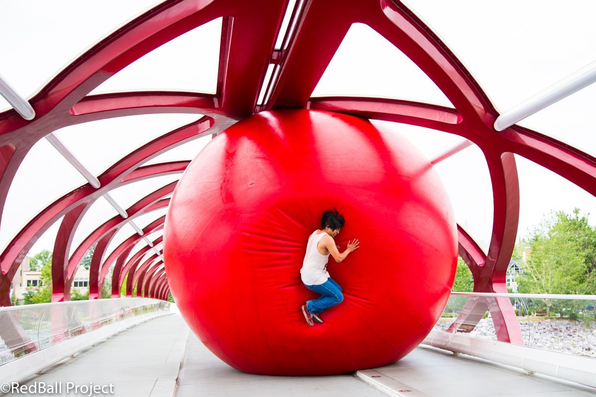 A child jumps into a gialt red inflatable ball in a city.