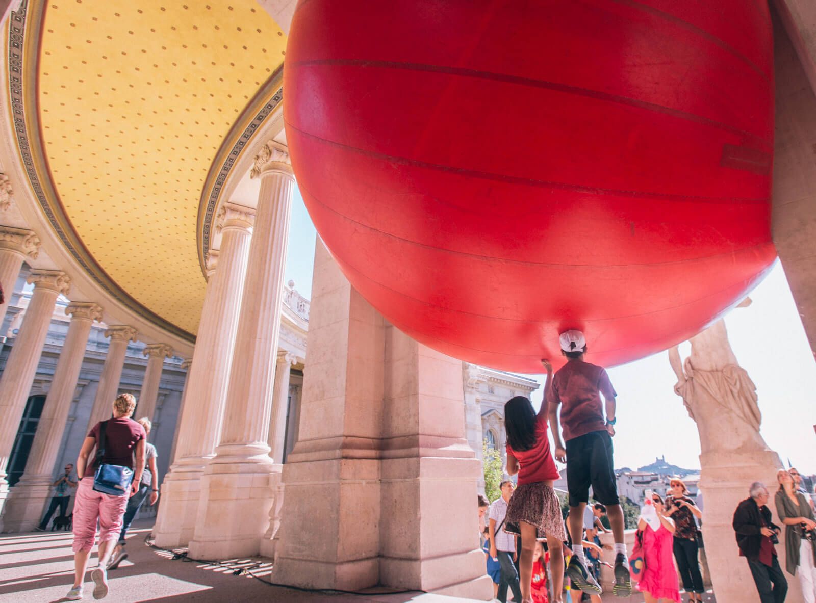 People jump to touch a large inflatable red ball suspended in the air.