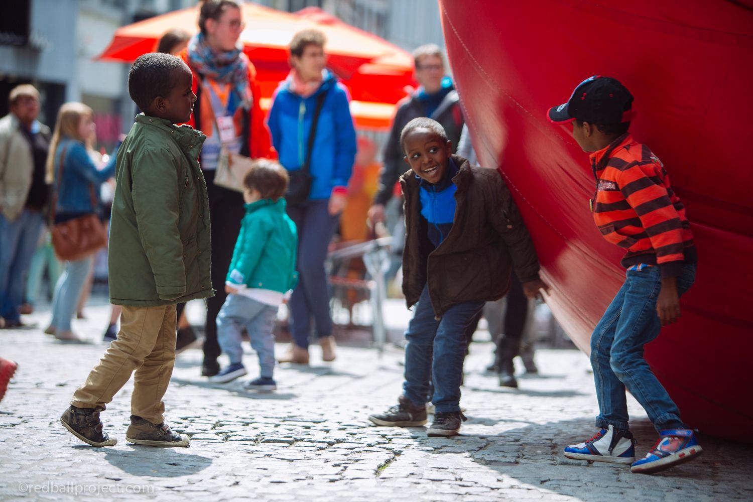 A child smiles while leaning against a large red inflatable ball.