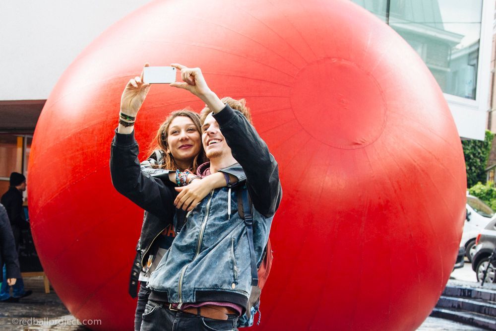 Two people take a selfie infront of a large red inflatable ball