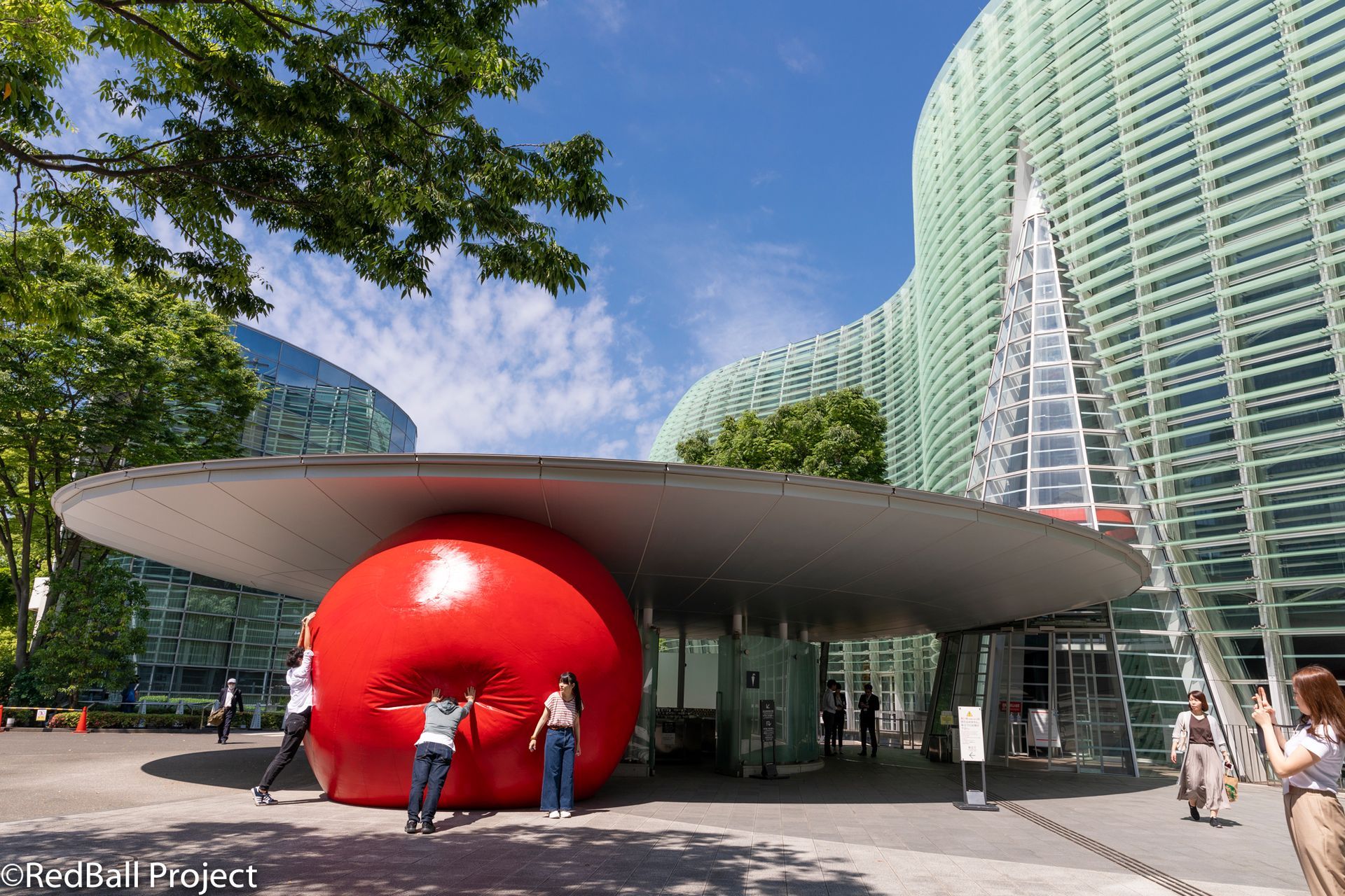 People lean on a large red inflatable ball in a city.